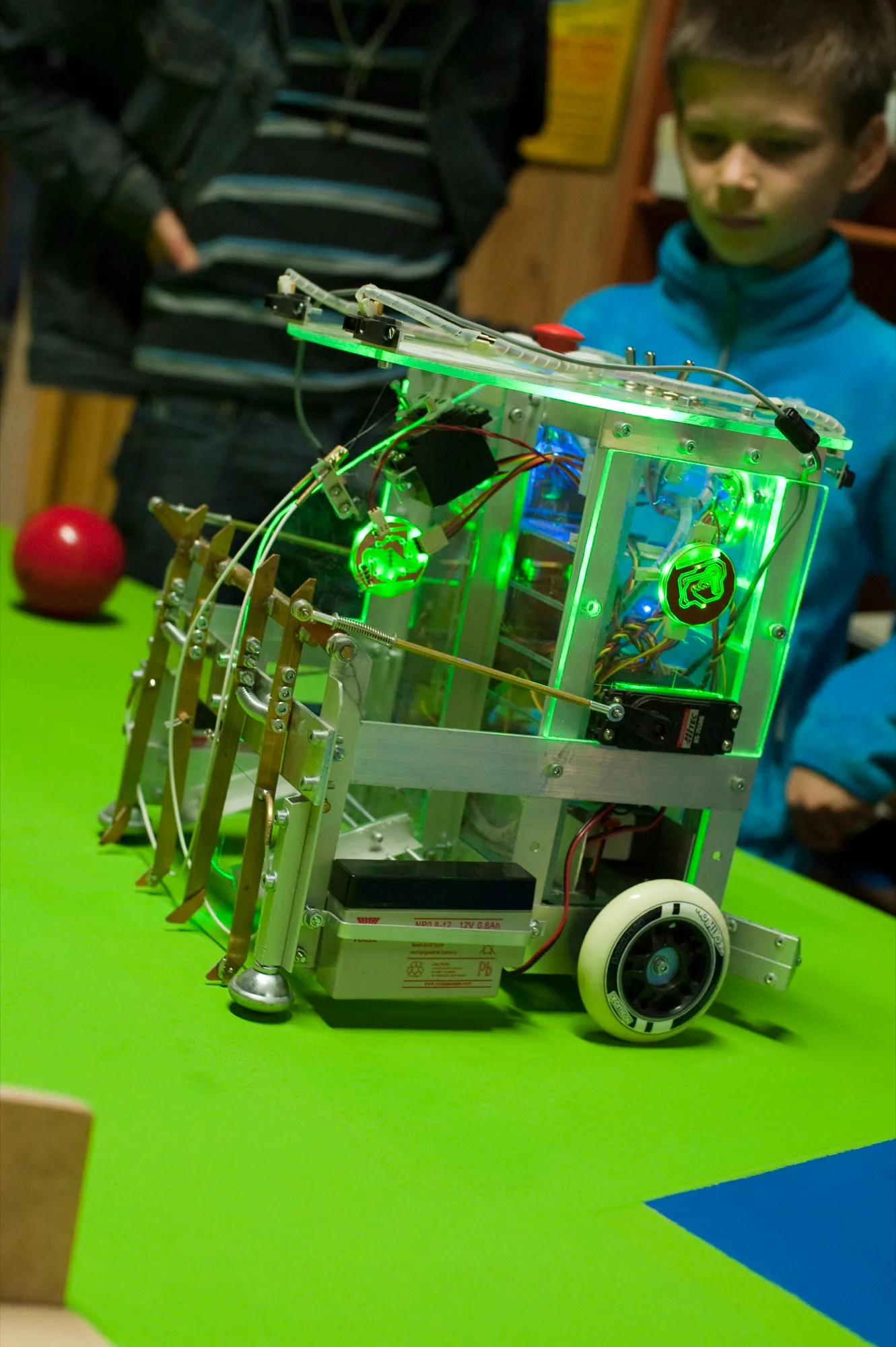GreenBot éclairé en vert sur une table de jeu, avec sa lame à rouleaux à l'avant