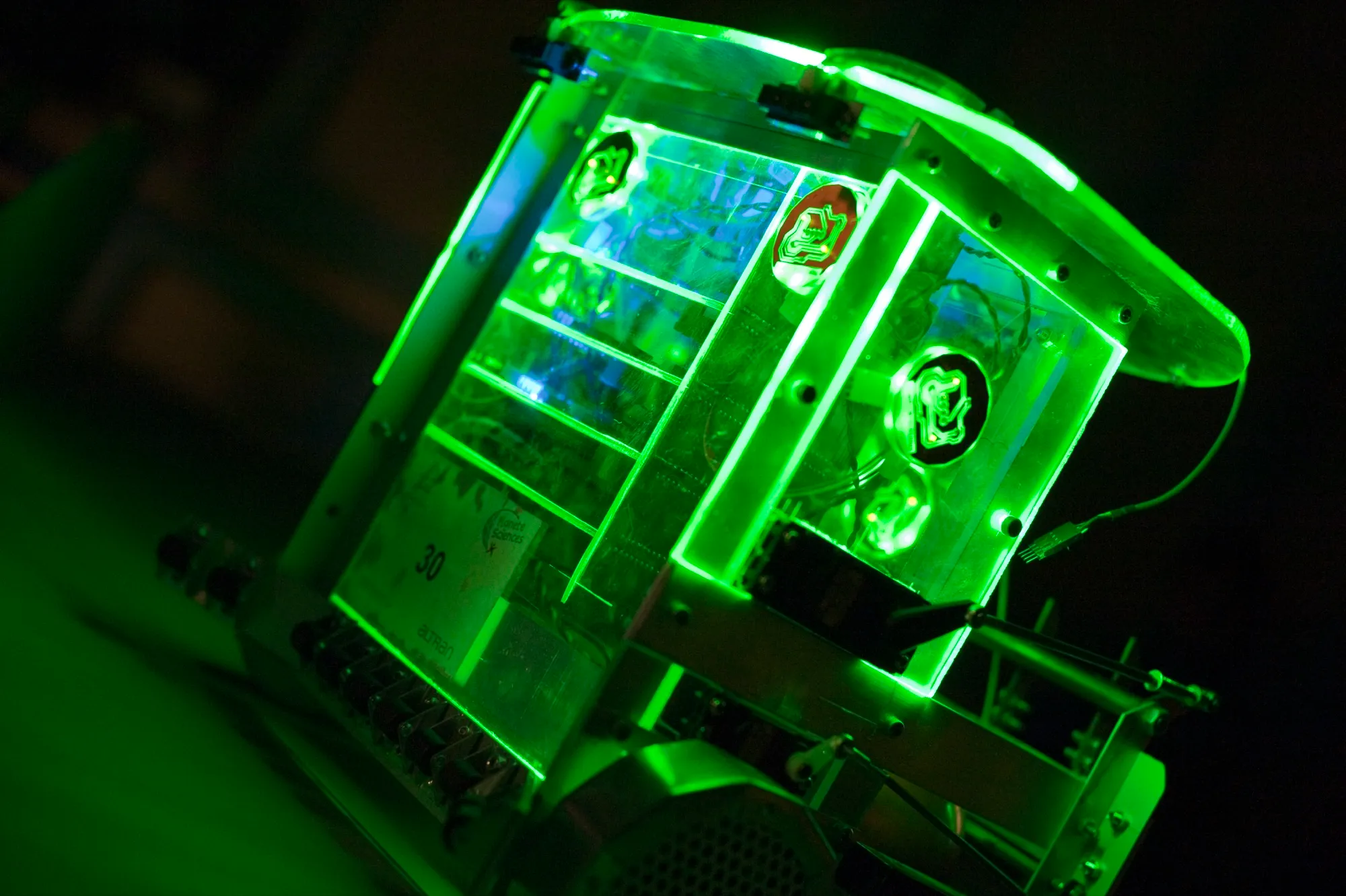Gros plan de GreenBot dans la pénombre, structure transparente éclairée en vert