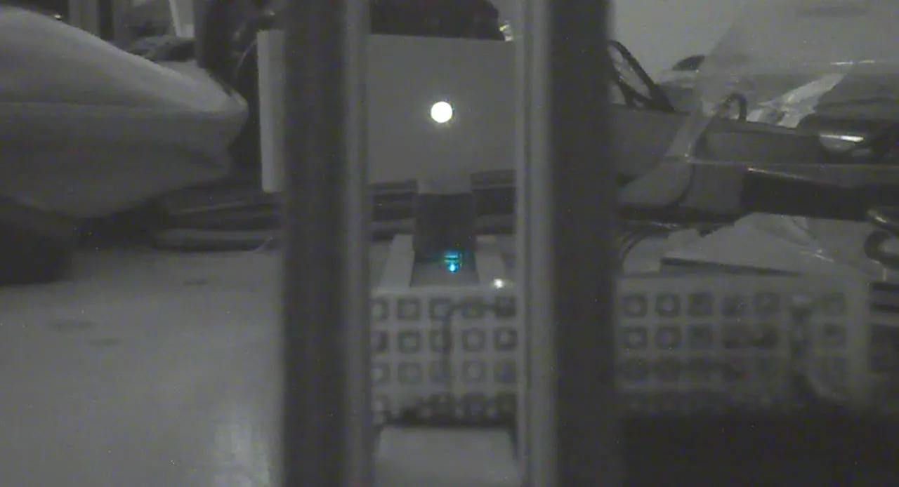 Image de webcam en noir et blanc : un point lumineux sur un mur blanc, posé sur le servomoteur du banc